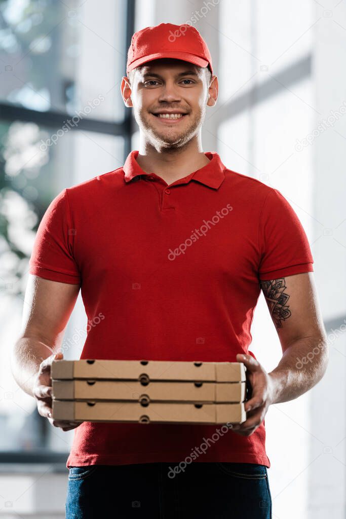 cheerful delivery man in cap and uniform holding pizza boxes 