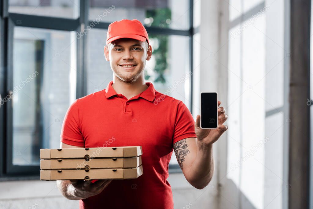 happy delivery man in cap holding smartphone with blank screen and pizza boxes 