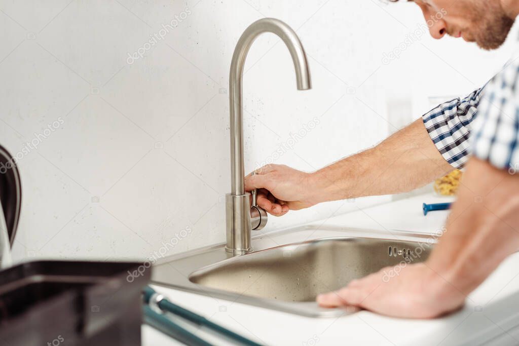 Cropped view of plumber fixing faucet near toolbox in kitchen 