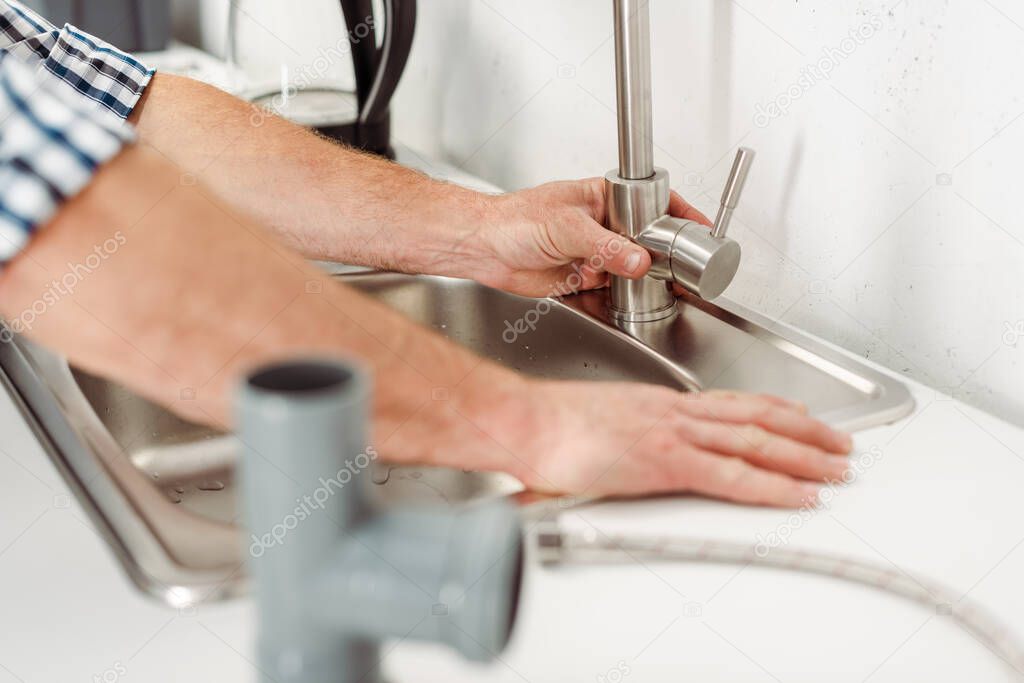 Selective focus of plumber fixing kitchen faucet near pipes on worktop 