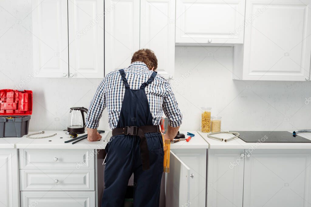 Back view of plumber in overalls working in kitchen 