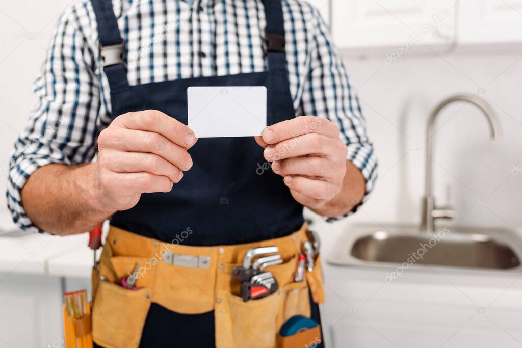 Cropped view of workman in tool belt holding empty card in kitchen 