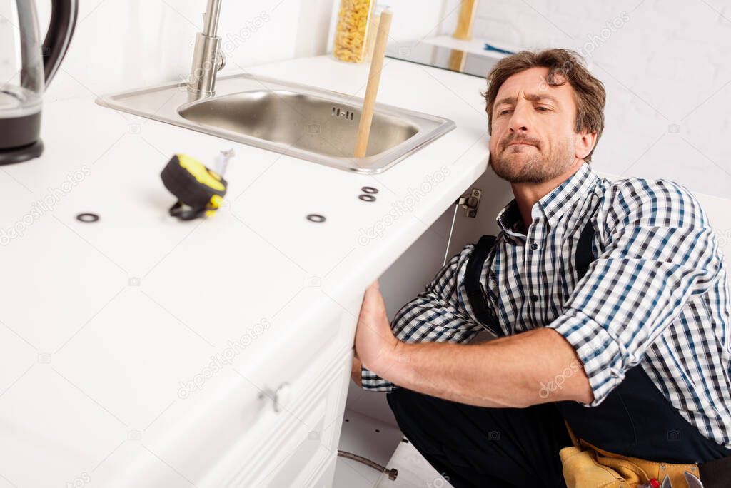 Selective focus of handsome workman fixing kitchen sink near industrial measuring tape on worktop 