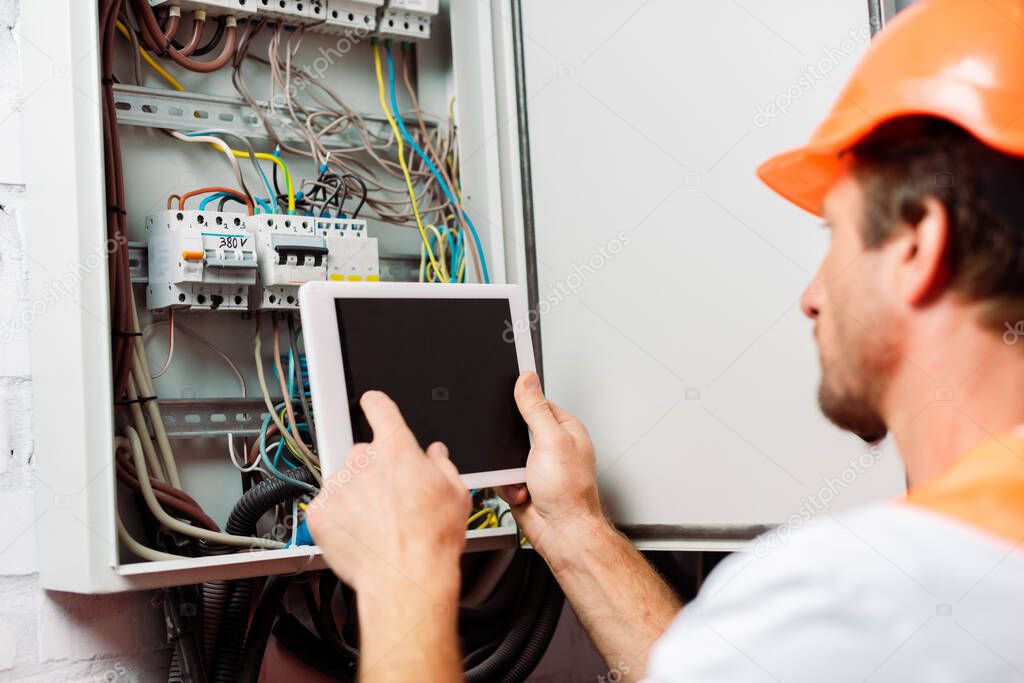 Selective focus of electrician using digital tablet with blank screen near electrical distribution box