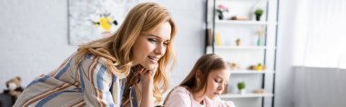 Evde çocuğun yanında duran gülümseyen bir kadının panoramik görüntüsü. 