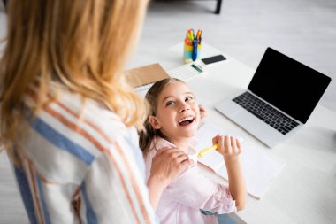 Pozitif çocuğun annesine bakıp dizüstü bilgisayarını ve defterini masanın yanında tuttuğu seçmeli odak noktası. 