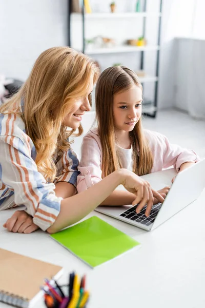 在家庭网络研讨会上 笑着母亲在女儿身边使用笔记本电脑的选择性焦点 — 图库照片