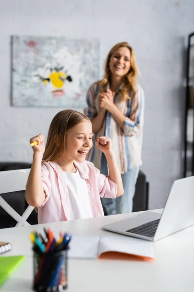 笑顔の子供の選択的な焦点は 自宅で正の母親の近くにオンライン教育の間にええジェスチャーを示す — ストック写真