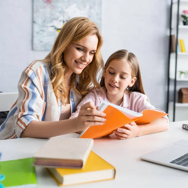 有选择性地专注于微笑的母亲和孩子在笔记本电脑和桌上的书本旁边看 — 图库照片