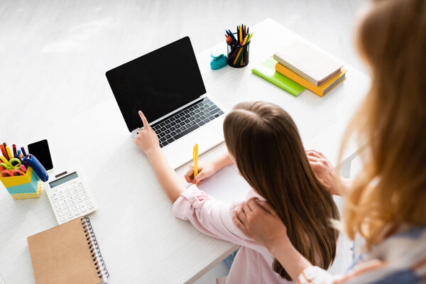 Overhead view of woman hugging daughter pointing with finger at laptop during electronic learning at home 