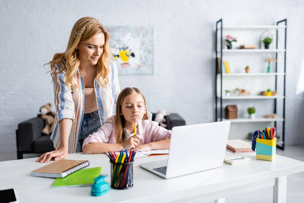 Selective focus of mother standing near thoughtful daughter during online education 