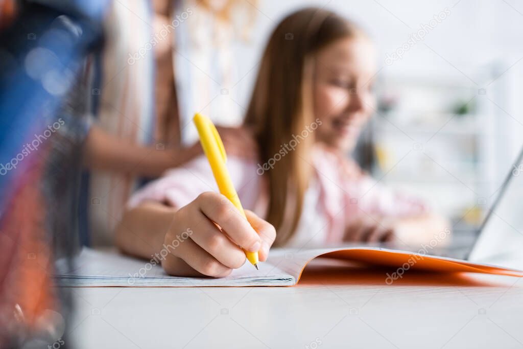 Selective focus of kid writing on notebook during electronic learning near mother  