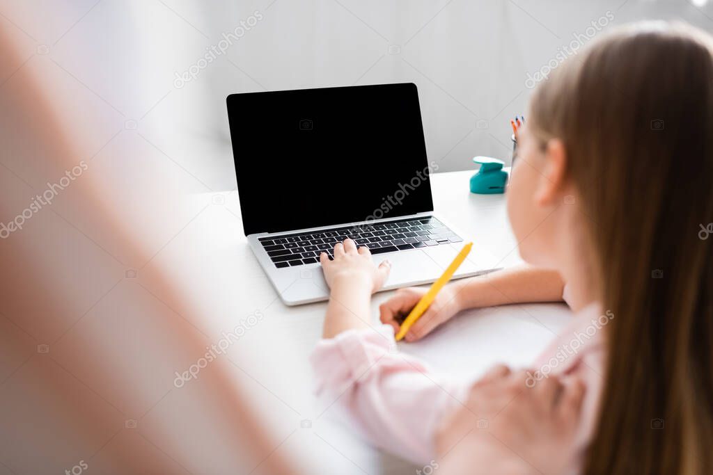 Selective focus of mother standing near daughter using laptop and writing on notebook 