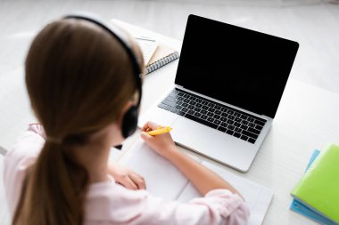 Evde online eğitim görürken, kulaklık takmış bir çocuğun deftere yazdığı genel bakış. 