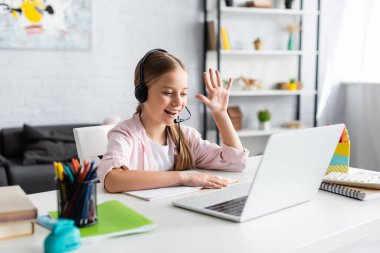 Evde Webinar sırasında kulaklık takmış, el sallayan pozitif çocuğun seçici odağı. 