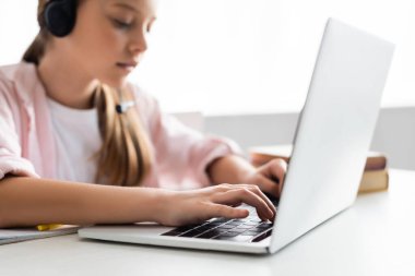 Kulaklıklı çocuğun evde dizüstü bilgisayarda yazışının seçici odağı 