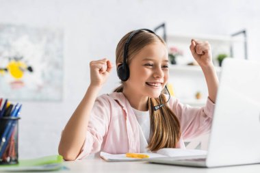 Evde çevrimiçi eğitim sırasında gülümseme gösteren kulaklıklı çocuğun seçici odağı 