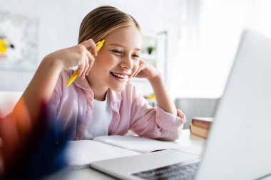 Not defterinin yanında elinde kalem tutan ve masadaki laptopa bakan pozitif çocuğun seçici odak noktası. 