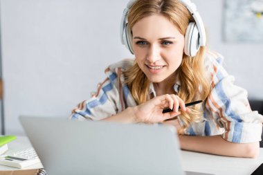 Dizüstü bilgisayar ve kulaklıklarla çalışan güzel bir yetişkin serbest çalışanın seçici odağı
