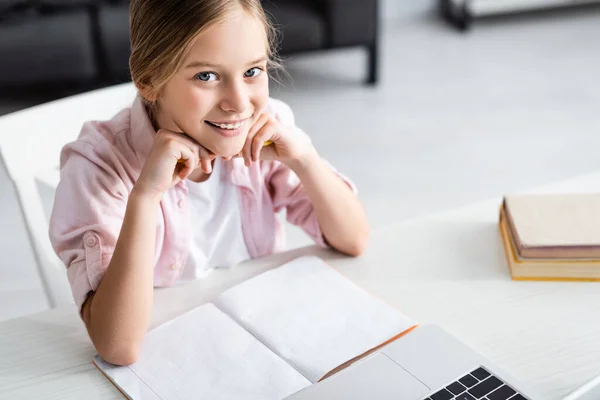 可爱的孩子在笔记本电脑旁的相机前微笑着 桌上放着一本书的高角镜头 — 图库照片