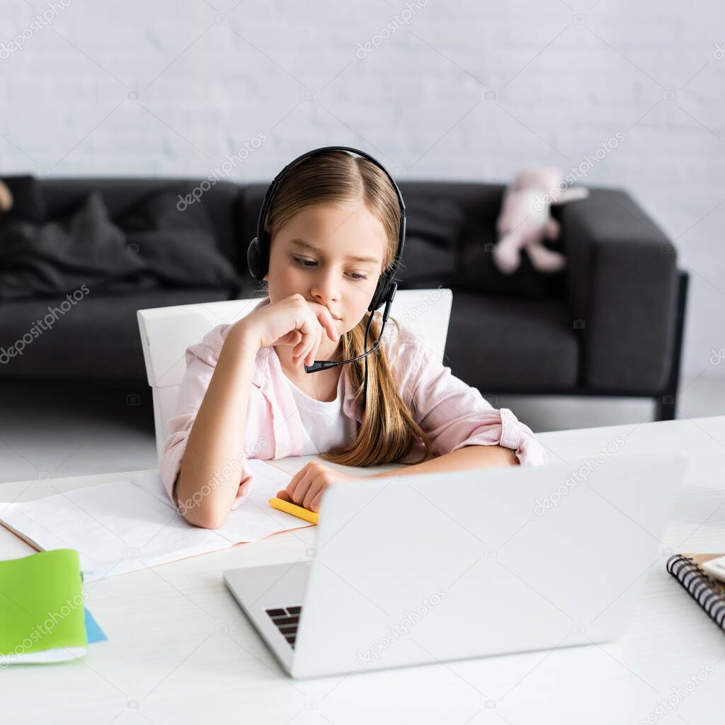 Selective focus of cute kid in headset sitting near notebook and laptop on table 