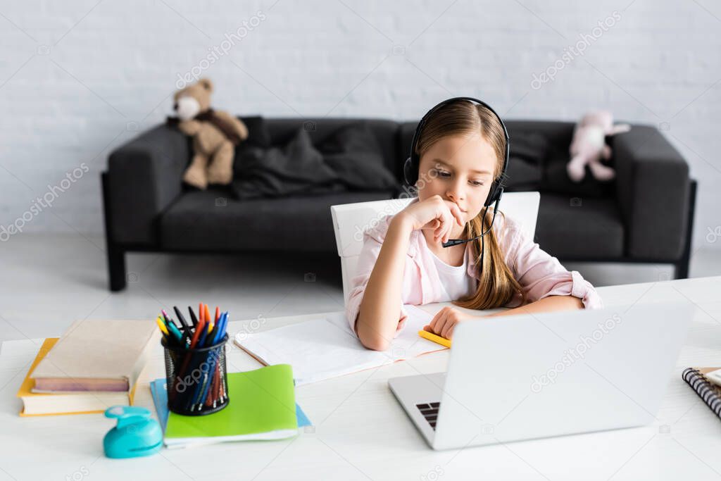 Selective focus of child using headset and laptop near books and stationery on table 