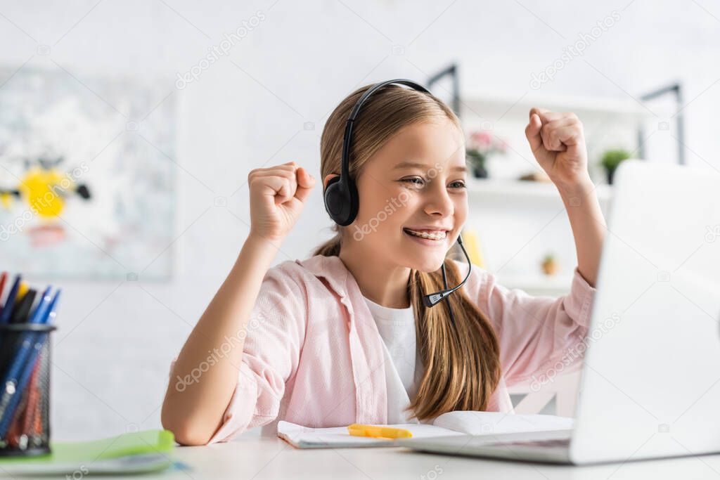 Selective focus of smiling child in headset showing yes gesture during online education at home 