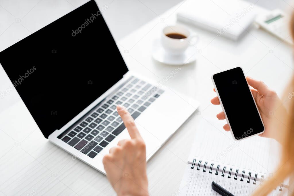 partial view of woman holding her gadget and working with laptop