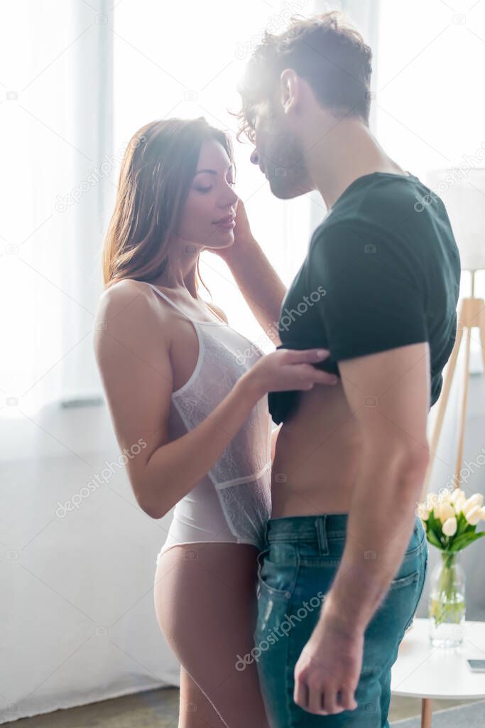 Selective focus of beautiful woman taking off shirt from handsome boyfriend at home 