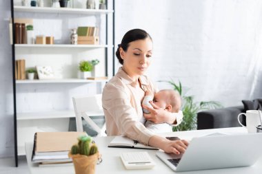 Evde dizüstü bilgisayar kullanırken annesinin bebeğini emzirdiği seçici odak noktası