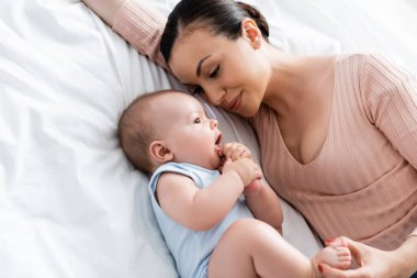 yüksek açılı anne yatakta uzanmış bebeğe bakıyor.
