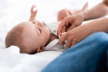 Seçici odak noktası, emziği olan tatlı bir çocuğa bebek tulumu giydirme.