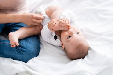 Annenin bebek tulumu giyip, oğlunun çıplak ayak emdiği seçici odak noktası.