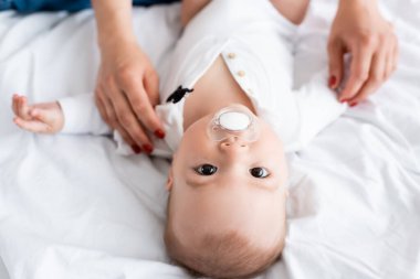 Annenin, emzik takan bir çocuğa bebek arabası giydirmesi.
