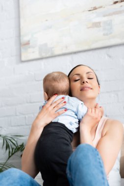 Güzel bir kadın, gözleri kapalı, tapılası bir erkek bebeği kucaklıyor. 