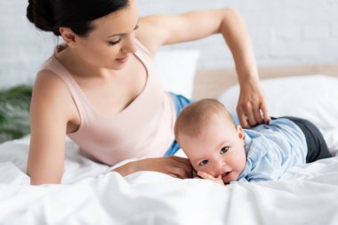 Annenin bebek elbiselerine dokunup bebek oğlunun yatağa uzanmasına odaklanması.