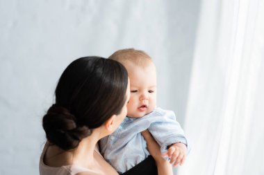 Anne kucağında kucağında bebek giysisi giymiş tatlı bir oğlan çocuğu. 