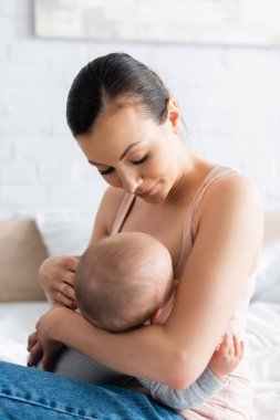 Anne yatak odasında emzirirken bebeğe bakıyor.