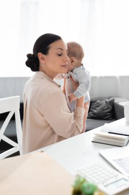 Annesinin seçici odağı, gözleri kapalı, kucağında tatlı bir oğlan çocuğu, masanın yanında.