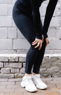 cropped view of sportswoman touching knees while exercising near brick wall  clipart