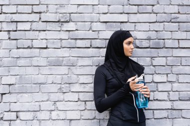 Siyah tesettürlü genç müslüman sporcu kadın elinde su şişesi tutuyor. 