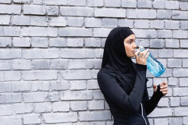 Genç müslüman sporcu kadın dışarıda su içerken spor şişesini tutuyor. 