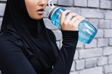 Türbanlı genç müslüman sporcu kadının spor şişesini dışarıda suyla tutarken çekilmiş görüntüsü. 