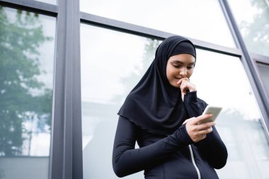 Zeki telefona bakan neşeli Müslüman kadının düşük açılı görüntüsü 