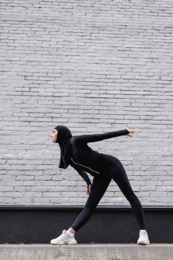 Türbanlı Arap sporcunun tuğla duvarın yanında egzersiz yaparken yan görünümü 