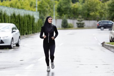 Arap sporcu kadın tesettür ve spor kıyafetleri içinde dışarıda koşuyor.