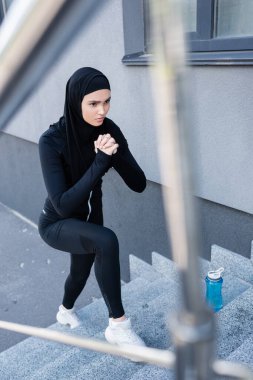 Spor şişesinin yanındaki merdivenlerde egzersiz yapan tesettürlü müslüman kadının seçici odağı 
