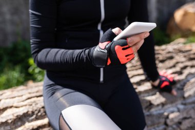 Dışarıda otururken elinde akıllı telefon tutan sporcu kadın manzarası. 