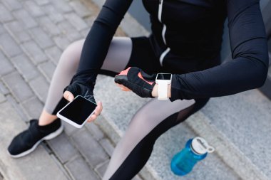 cropped view of young sportswoman with fitness tracker on hand holding smartphone with blank screen  clipart