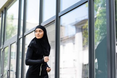 Binanın yakınında koşan tesettürlü ve spor kıyafetli Arap bir kız. 